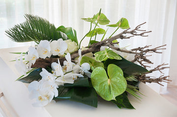 Rouwarrangement met bloemen en houtstronken. Een modern rouwstuk voor een uitvaart.