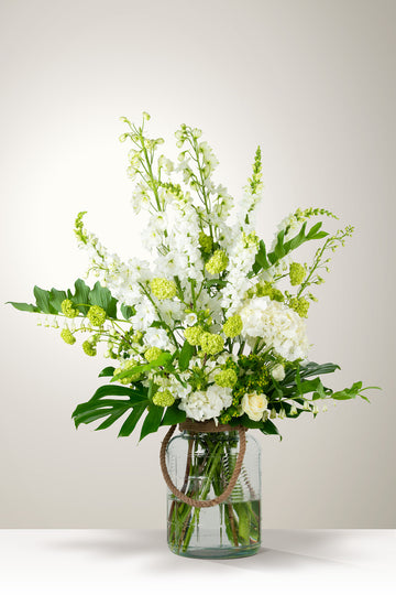 Witte bloemenvaas voor naast een kist. Bloemrijke decoratie uitvaart.